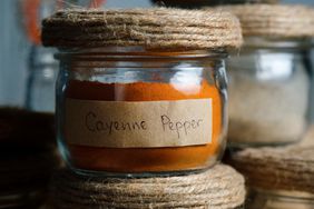 A composition of many different spices and herbs standing in a row on a wooden table or shelf. Dry crushed spices and seasonings in glass jars and containers with inscriptions, in the kitchen cabinet or pantry. The concept of cooking, home decor.