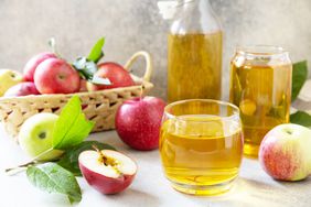 Glass of apple juice sitting next to basket of apples