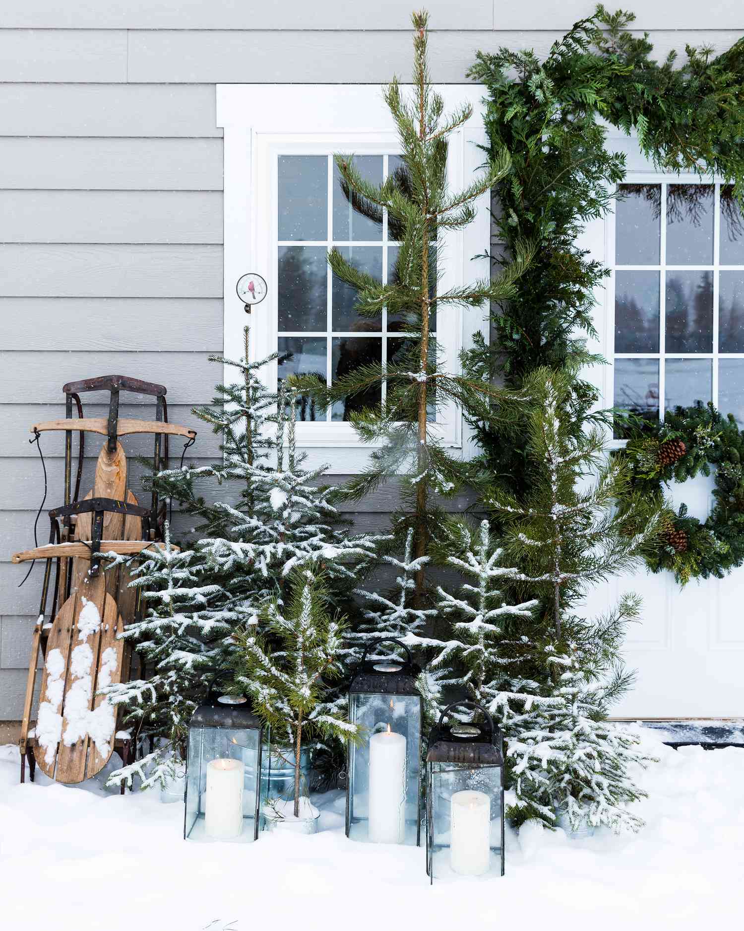 sled, trees and candles in snow near a house