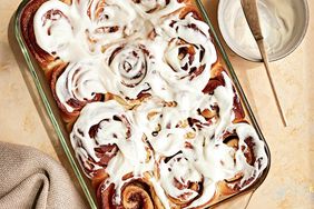 cinnamon rolls in glass pan with bowl of frosting