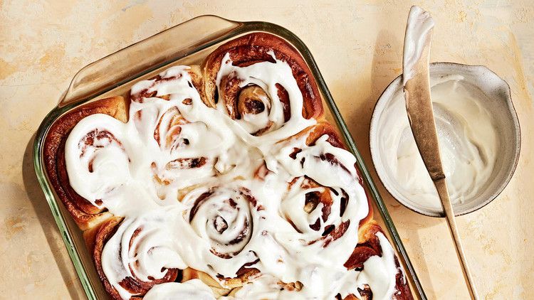 cinnamon rolls in glass pan with bowl of frosting