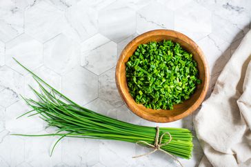 Fresh chopped green onions in a wooden bowl and a bunch of onions on the table. Top view.