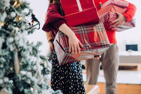 People holding wrapped Christmas presents standing next to a Christmas tree