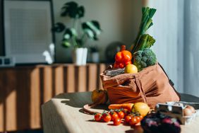 Eco-friendly reusable shopping bag with multi-coloured fresh vegetables and groceries on the table at home. Shopping with reusable grocery bag for plastic free and waste-free life. Responsible shopping. Zero waste and sustainable lifestyle concept