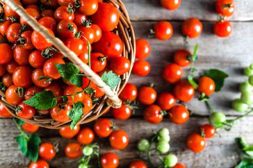 Basket of cherry tomatoes on wooden background, fresh produce on table