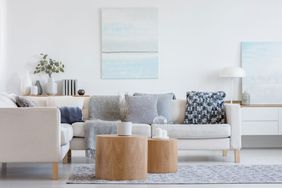 Two wooden coffee tables with plant in pot in front of grey corner sofa in fashionable living room interior