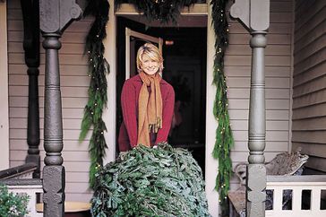 Martha Stewart holding a Christmas tree on a front porch