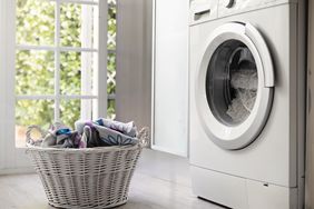 View of laundry room with washing machine and laundry basket with dirt clothes