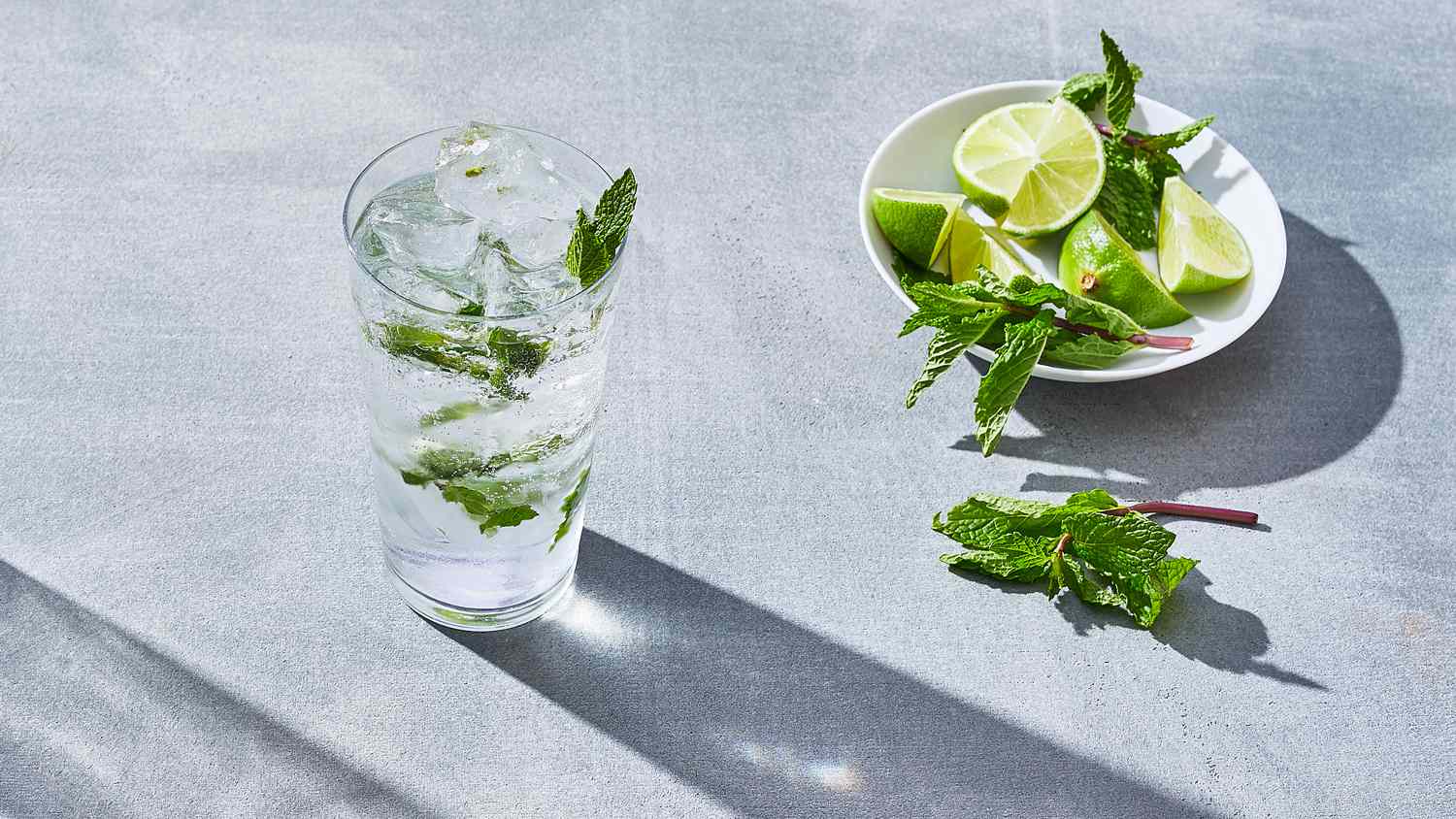 glass of mojito next to plate of limes