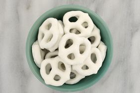 Top view of yogurt covered pretzels in a green bowl atop a gray marble cutting board.