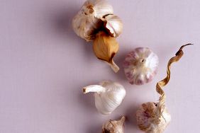 multiple garlic bulbs on a pale lavender surface