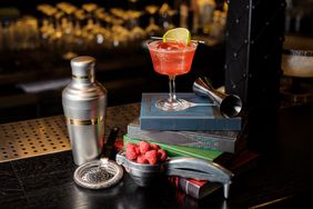 Glass filled with fresh sweet summer cocktail with lime slice on books, bar utensils and raspberries on the table