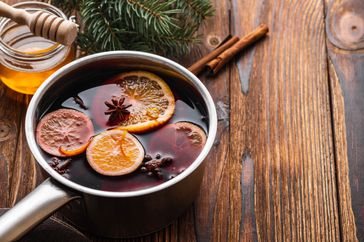 Mulled wine hot drink with citrus, apple and spices in aluminum casserole and Fir branch on background.