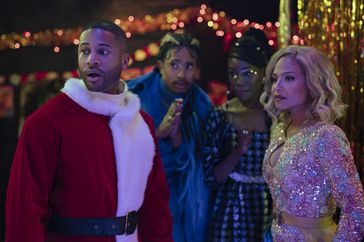 Man in a Santa costume with three people and Christmas lights.