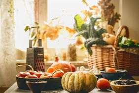 Pumpkin and various seasonal vegatbles and fruits in basket and bowls on kitchen table at window background