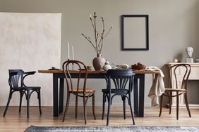 rustic interior of dining room with walnut wooden table, retro chairs, decoration, fireplace, dried flower, candlestick mock up picture frame and carpet