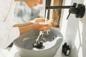 Young woman awakening, washing and cleaning her face with splashing water.