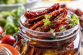 Sun-dried tomatoes marinated in olive oil with herbs and olives in a jam jar.