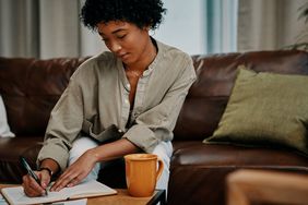 woman writing in journal sitting on sofa